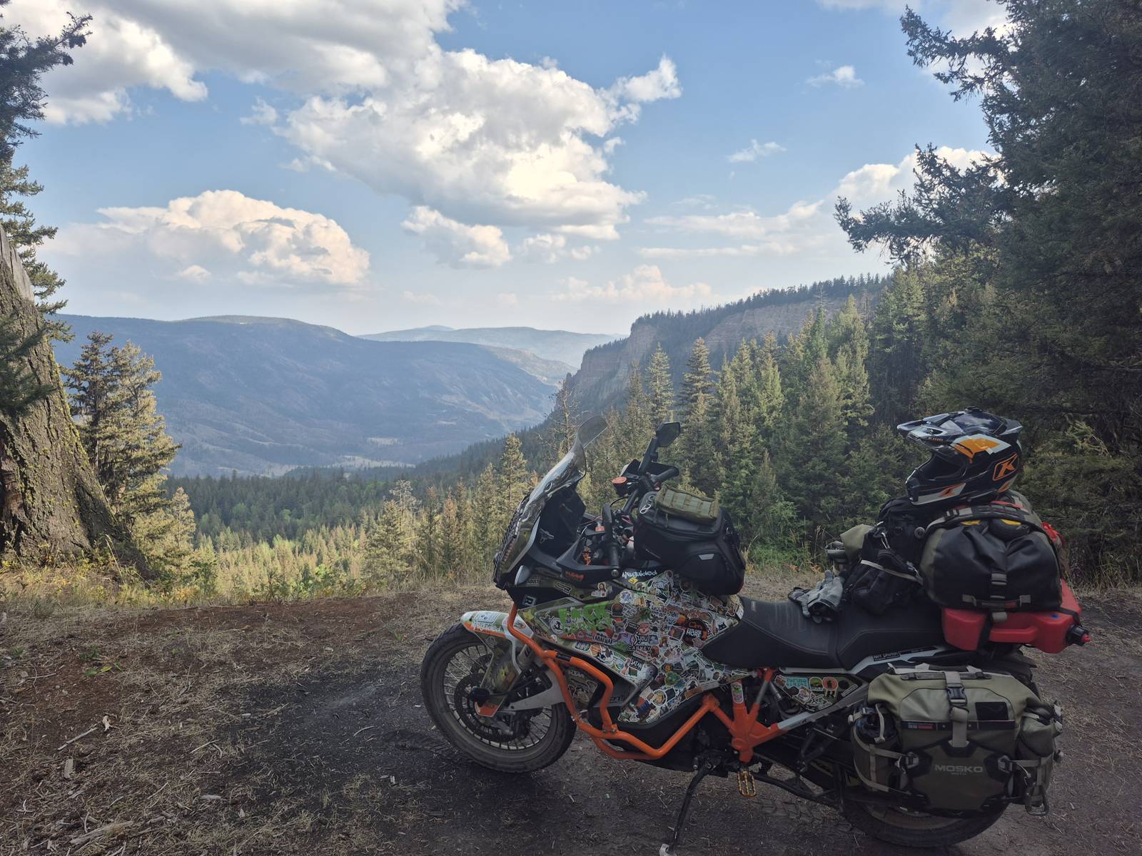 Loaded adventure motorcycle at a cliff-edge viewpoint over a forested canyon valley