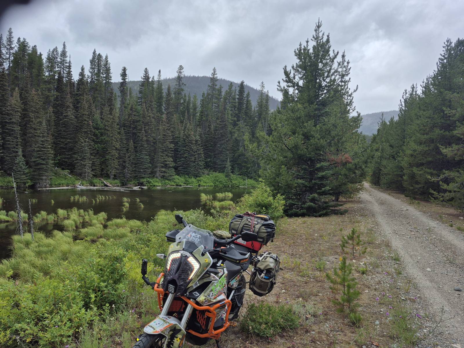 Loaded adventure motorcycle on a gravel road beside a forest lake