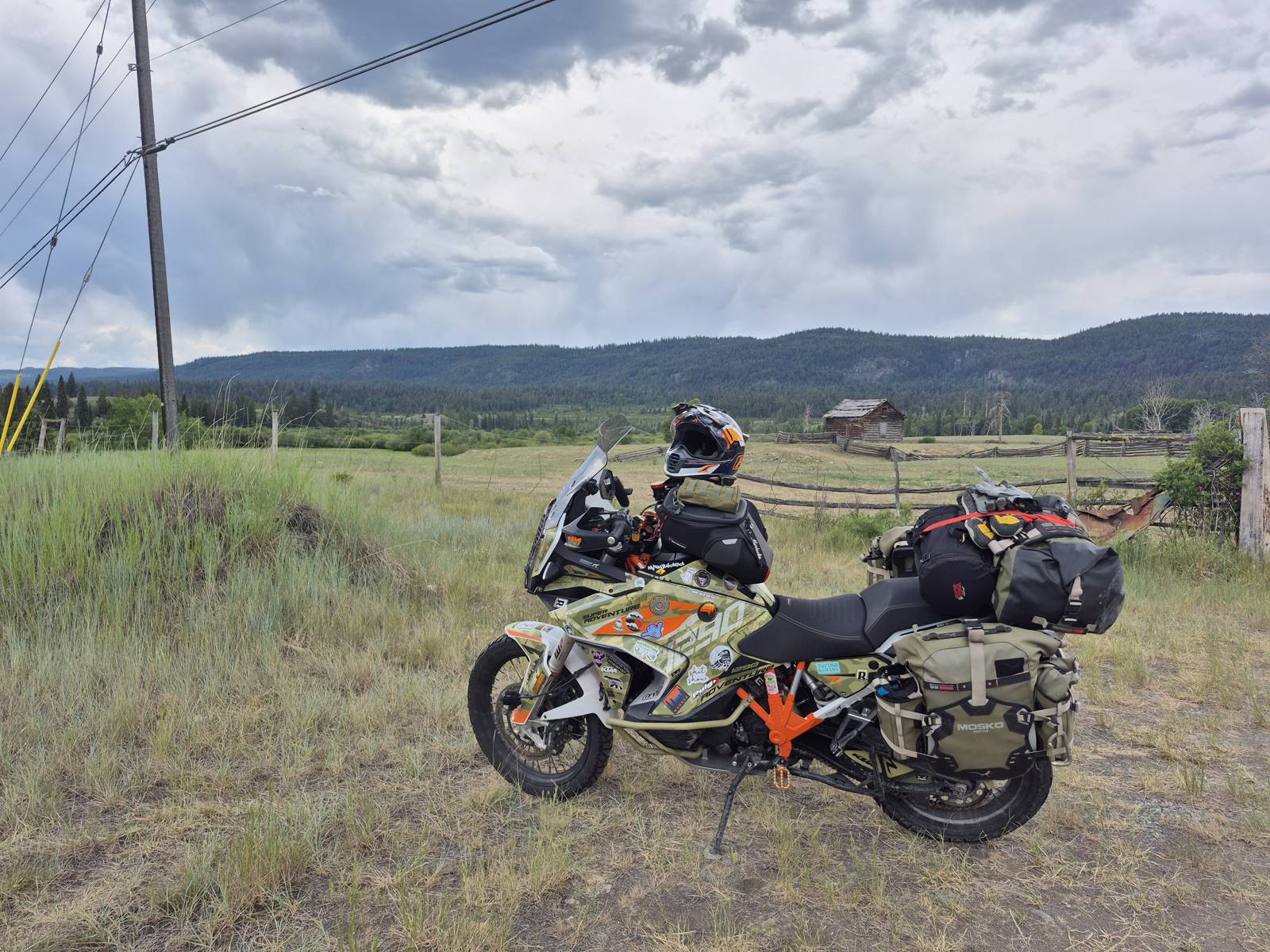 Motorcycle by a fenced field with an old log cabin under a stormy sky